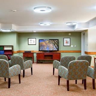 A waiting room with comfortable chairs facing a television and decorated with framed artwork.