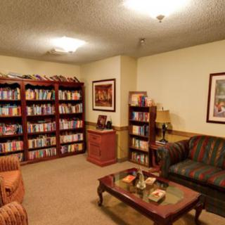 A cozy library room with bookshelves, comfortable seating, and warm lighting.