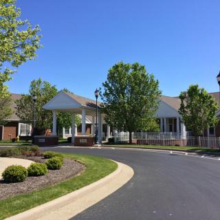 A suburban residential building with a driveway surrounded by trees and landscaping.