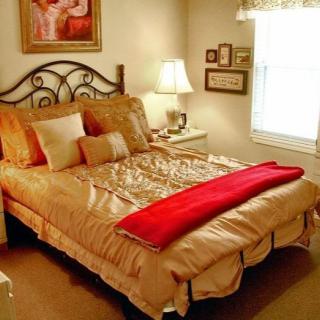 A cozy bedroom with a neatly made bed, accented by a red blanket and soft lighting.