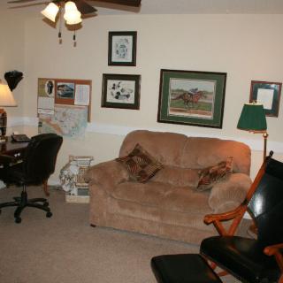 A cozy living room featuring a sofa, armchair, desk with an office chair, and framed pictures on the wall.