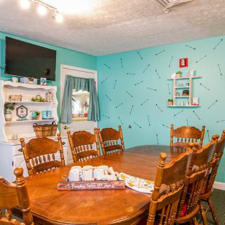 A cozy dining room with a wooden table and chairs, decorated with turquoise walls and a television.