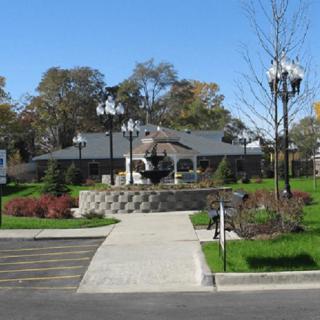 A building with a landscaped garden featuring a central fountain, surrounded by trees and lamp posts.