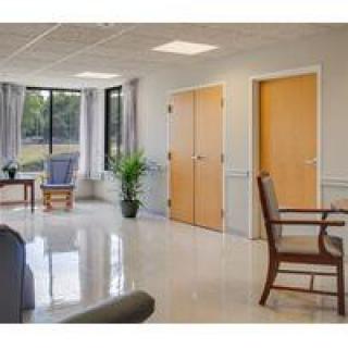 A bright and clean waiting room with chairs, a table, and a potted plant near large windows.