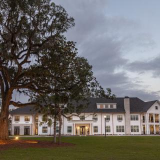 A large white residential house with a well-maintained lawn and a prominent tree at twilight.