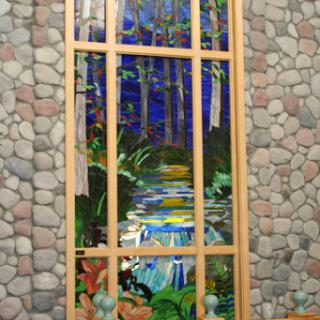 A beautifully crafted stained glass window depicting a serene forest scene with flowing water.
