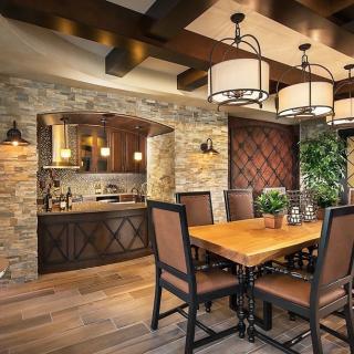A rustic dining room with stone walls, wooden furniture, and elegant chandeliers creating a warm and inviting atmosphere.