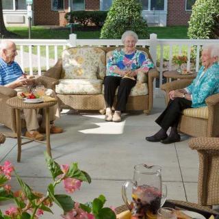 A group of elderly people socializing on a patio with comfortable furniture and plants.