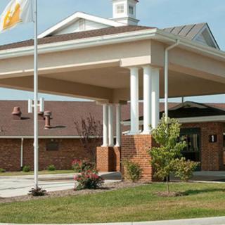 A brick building entrance with columns and an overhang, featuring a flag and landscaping.