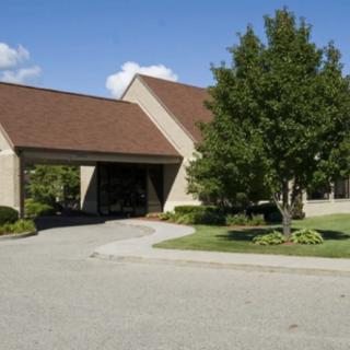 A church building with a sloped roof, surrounded by greenery and a paved driveway.