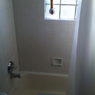 A small bathroom with a bathtub, tiled walls, and a window above the showerhead.