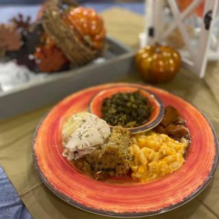A plate of comfort food with mac and cheese, greens, mashed potatoes, and fried chicken surrounded by autumn decorations.