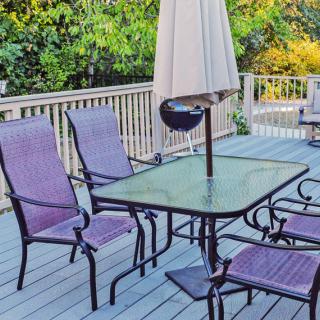 A tranquil patio setup with a glass table and chairs under an umbrella on a wooden deck.