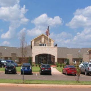 A view of a building with an American flag in front and cars parked in the lot.