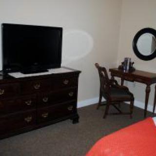 A cozy bedroom with a television on a dresser and a small desk with a round mirror.