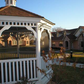 A gazebo in a garden setting with houses in the background on a sunny day.