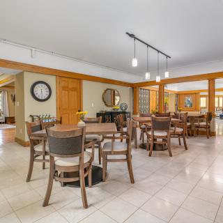 A spacious dining area featuring multiple tables and chairs, with stylish lighting and decorative elements such as a wall clock and mirror.