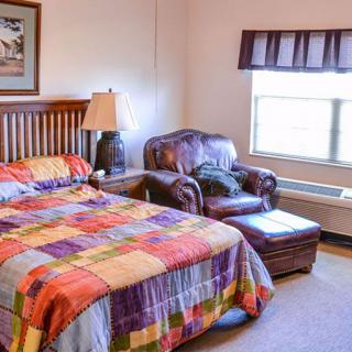 A cozy bedroom with a colorful quilt on the bed and an armchair by the window.