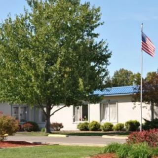A single-story building with a blue roof, surrounded by a tree and an American flag in the foreground.