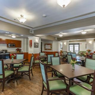 A spacious and well-lit dining room with multiple tables and chairs, adjacent to a kitchen area.