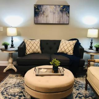 A cozy living room with a dark sofa, patterned pillows, soft lighting from table lamps, and a round coffee table.