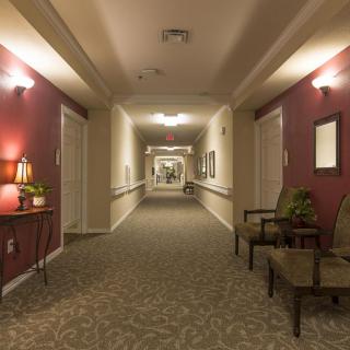 A well-lit hotel hallway with chairs and decorative lamps along the walls.