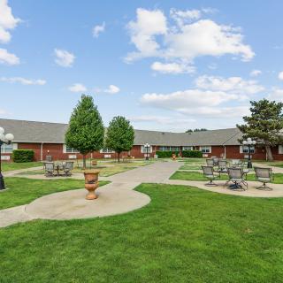 A landscaped courtyard with pathways, benches, and trees under a partly cloudy sky.