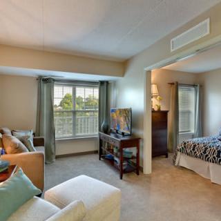 A cozy apartment interior featuring a living room with a TV and sofa, adjacent to a bedroom area.