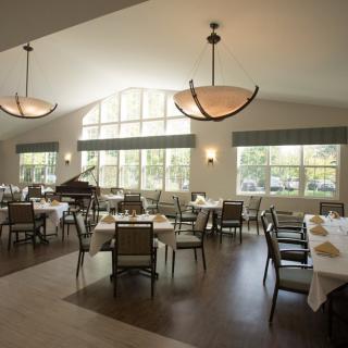 A spacious dining room with neatly arranged tables and chairs, featuring large windows and a grand piano.