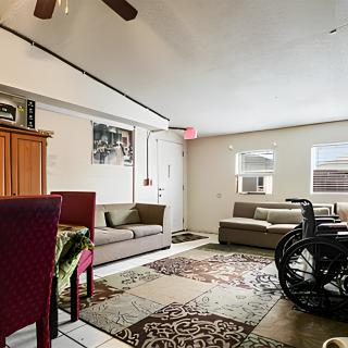 A cozy living room with sofas, a wheelchair, and decorative rugs.