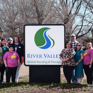 A group of staff members proudly posing in front of the River Valley Skilled Nursing & Therapy sign.