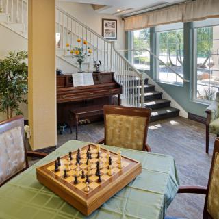 A cozy indoor setting featuring a chess board on a table, with a piano and stairway in the background.