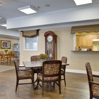A cozy dining area with a table and chairs, adjacent to a kitchen, featuring a wooden floor and a grandfather clock.