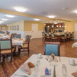 A well-lit dining area featuring neatly arranged tables and chairs, with a bar in the background.