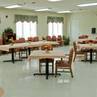 An empty dining room with several tables and chairs, decorated with flowers and natural light streaming through the windows.