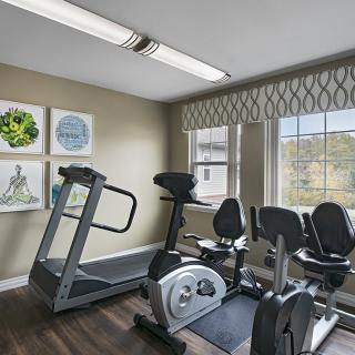 A small home gym with a treadmill and stationary bike, featuring natural light from large windows.