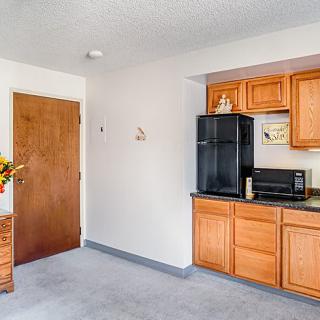 A small kitchenette with wooden cabinetry, featuring a fridge and microwave, and a flower arrangement on a side table.