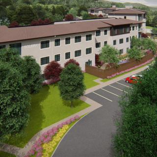 Aerial view of a modern building surrounded by greenery and a parking lot.