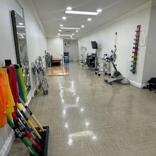 A well-lit gym space featuring various exercise equipment and rehabilitation tools along a spacious hallway.