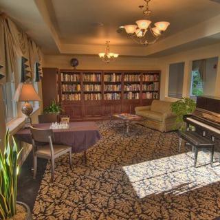A cozy library room featuring a bookshelf, piano, and comfortable seating.