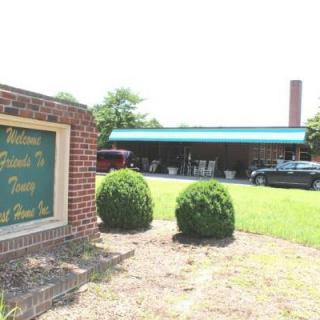 A restaurant with a brick sign and green awning, surrounded by neatly trimmed bushes.