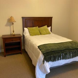 A neatly arranged bedroom with a wooden bed, green pillows, and a matching blanket.