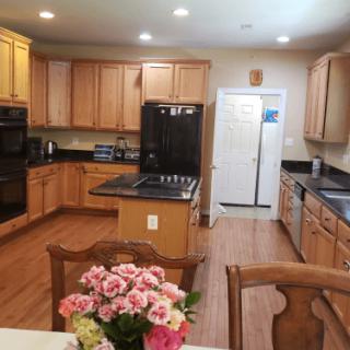 A spacious kitchen with wooden cabinets, black appliances, and a dining area featuring a vase of flowers.