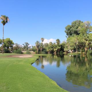 A picturesque golf course with a tranquil pond and lush greenery under a clear blue sky.