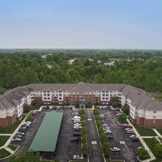 Aerial view of a residential apartment complex surrounded by trees, featuring a spacious parking lot.