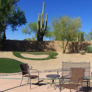 A relaxing patio setup with chairs and a table overlooking a desert landscape featuring cacti and trees under a clear blue sky.