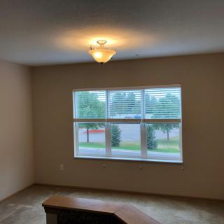 A view of an empty room with a ceiling light fixture and a large window overlooking the outdoors.
