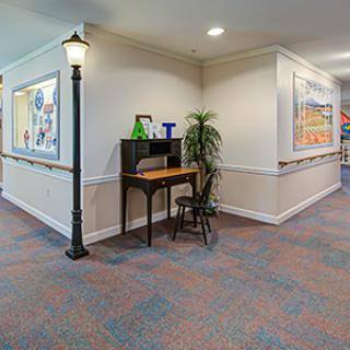 A hallway with a small desk and chair, featuring artwork on the walls and a decorative lamp post.