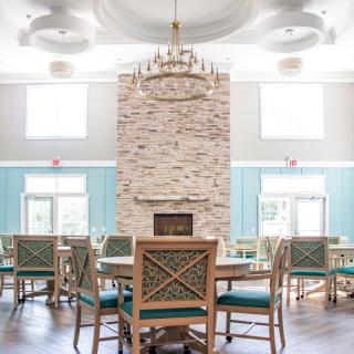 A spacious dining room featuring a stone fireplace, elegant chandelier, and stylish wooden furniture in a bright, light-filled space.