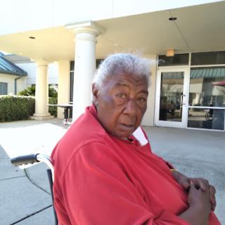 An elderly person sitting outside a building, dressed in red.